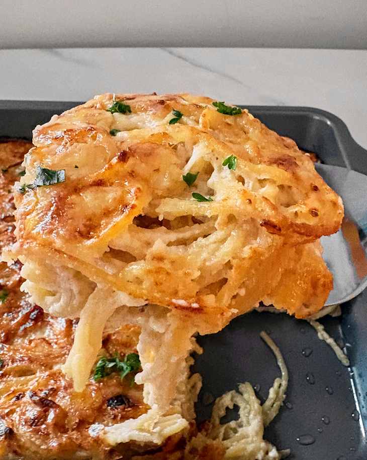 Closeup of spatula with a serving of Alfredo Baked Spaghetti in front of a pan