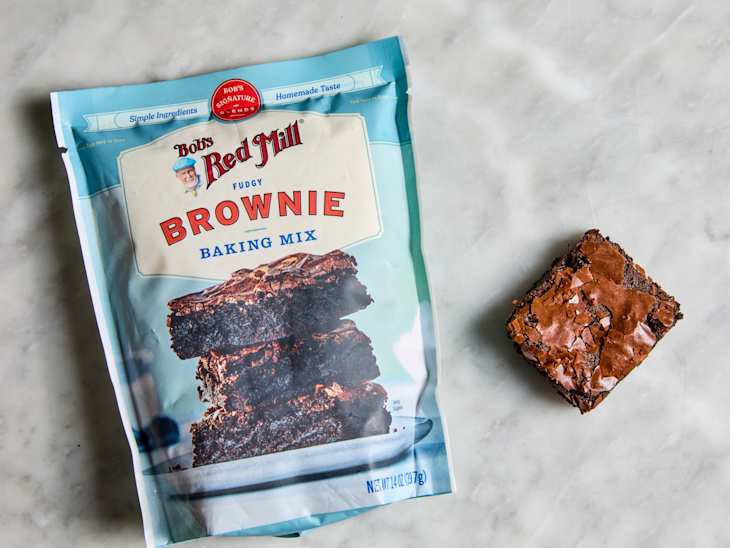 Bob's Red Mill Fudgy brownie mix package next to a baked brownie square on a marble surface.