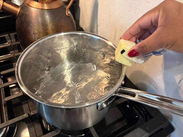 Someone rubbing butter on side of a pot of boiling water.