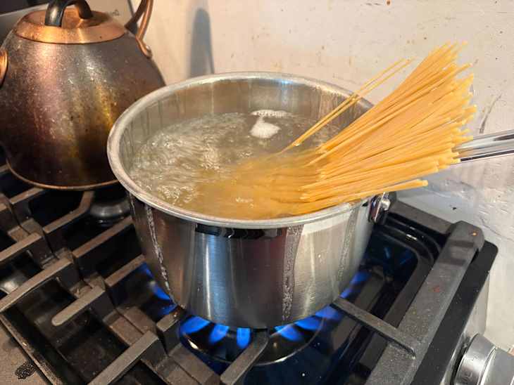 Boiling water coming out of the sides of a pot of pasta being cooked.