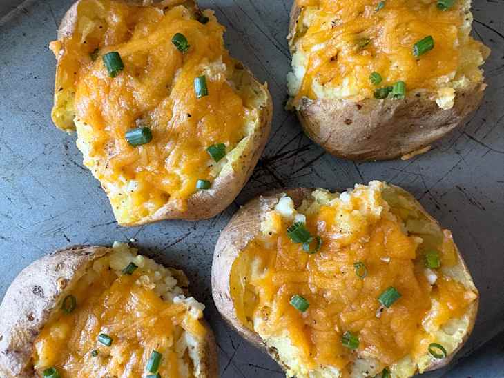 Baked potatoes topped with melted cheddar cheese and chopped green onions on a baking sheet.