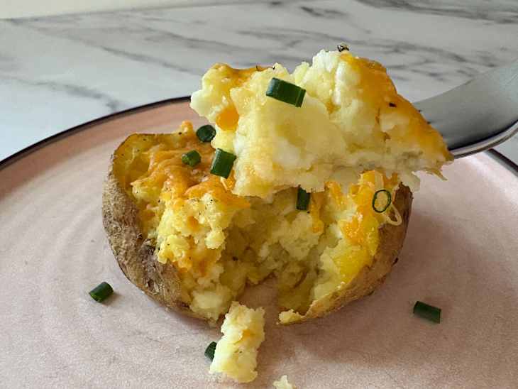 Baked potato topped with melted cheese and chopped green onions, served on a pink plate.