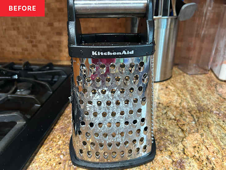 Stainless steel box grater with water droplets, placed on a granite countertop near a gas stove.