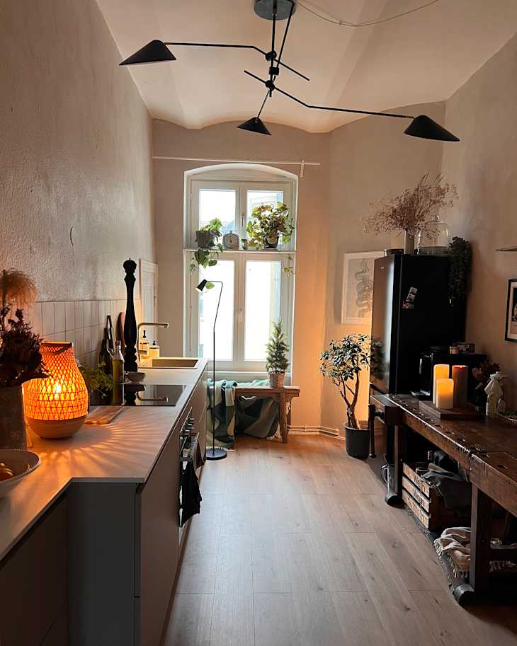 Cozy kitchen with a modern design, featuring a wooden table, plants, and warm lighting from a decorative lamp.