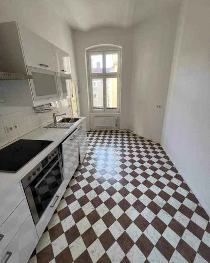 Modern kitchen with white cabinets, a black cooktop, and a checkered brown and white floor. Large window provides natural light.