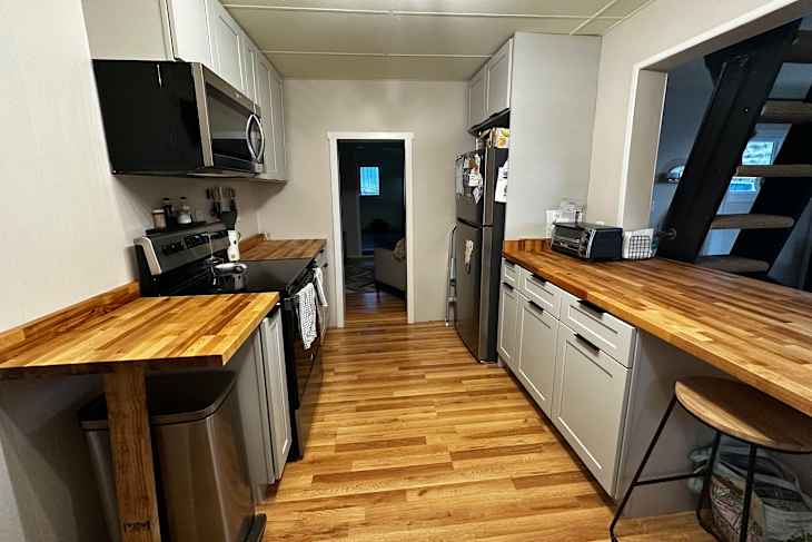 Modern kitchen with wooden countertops, stainless steel appliances, and a small bar stool.