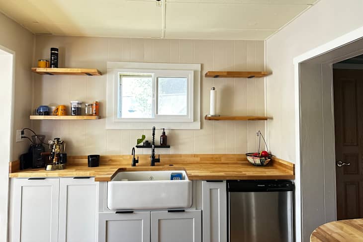Modern kitchen with a farmhouse sink, wooden countertops, open shelves, coffee equipment, and a fruit basket.