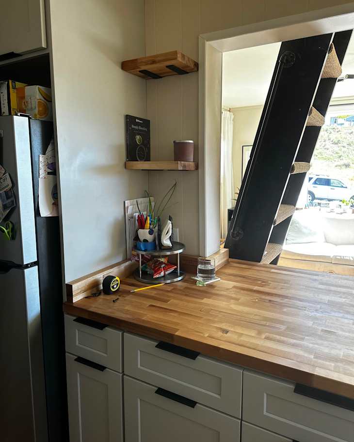 Wooden countertop in a kitchen with shelves, a glass of water, and office supplies on a circular stand.