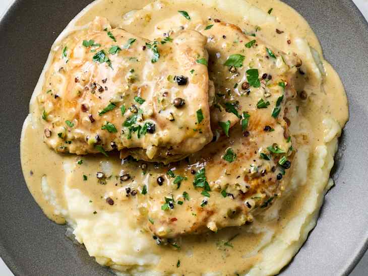 A close up of chicken au poivre on top of mashed potatoes in a gray bowl