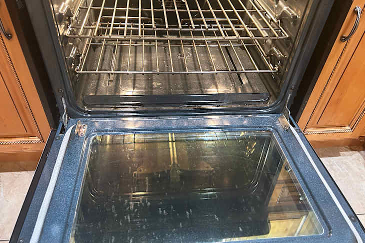 Oven interior with metal racks, glass door, and visible dirt on the bottom surface.
