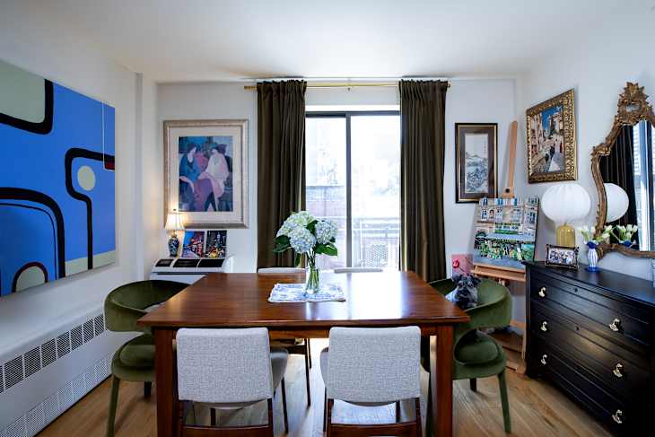 Dining room featuring a wooden table, green velvet chairs, floral centerpiece, and colorful artwork on the walls.