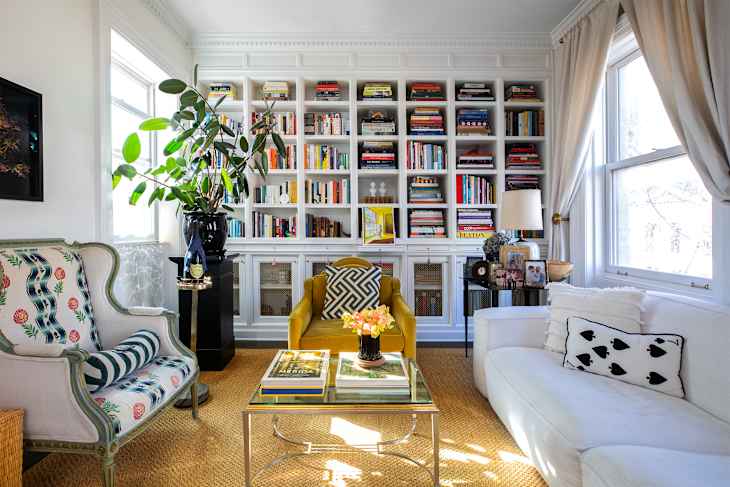 Cozy living room with a yellow armchair, white sofa, patterned armchair, and a bookshelf filled with books.