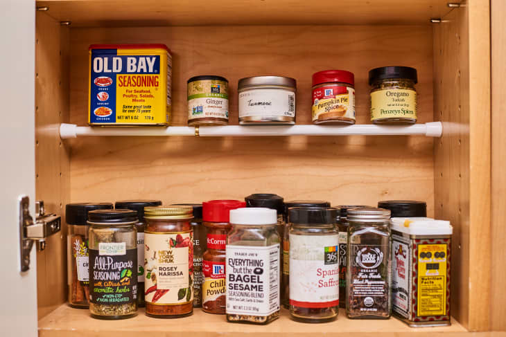 A tension rod is built inside of a cabinet for housing spices, small jars, and boxes of specialty seasonings