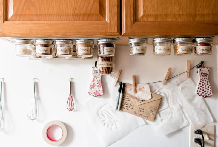 Spices are stored in small jars and affixed with magnets to a strip on the underside of cabinets