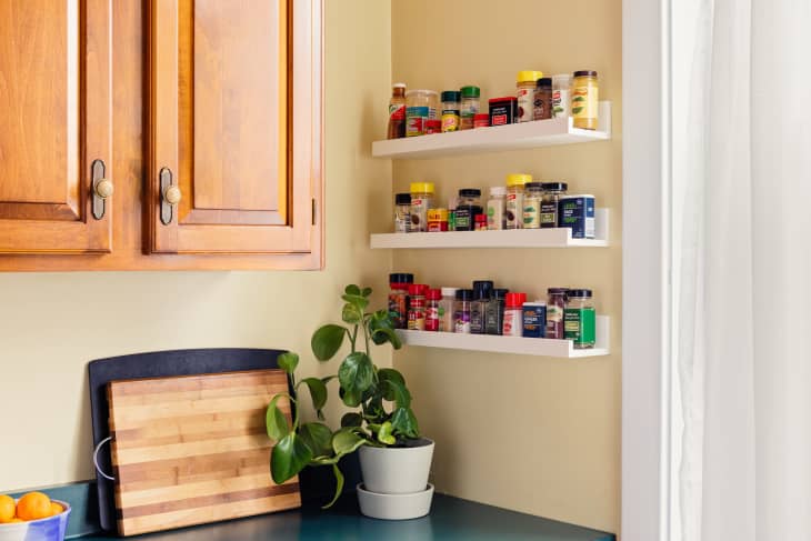 Wooden kitchen cabinets, spice jars on white shelves, cutting board, and potted plant on countertop.