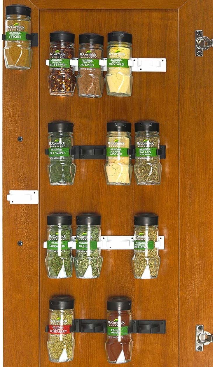 Wooden cabinet door with mounted spice rack holding various McCormick spice jars, including cumin, nutmeg, and basil.