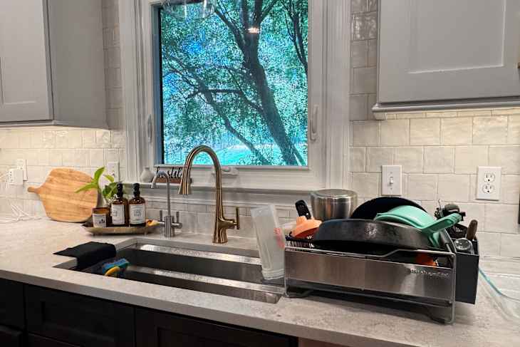 Kitchen sink area with dish rack holding clean dishes, and a wooden cutting board.