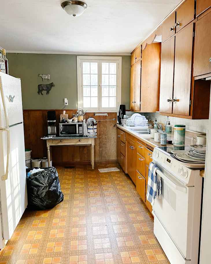 Kitchen with wooden cabinets, patterned linoleum floor, white appliances, and a small table with a microwave.