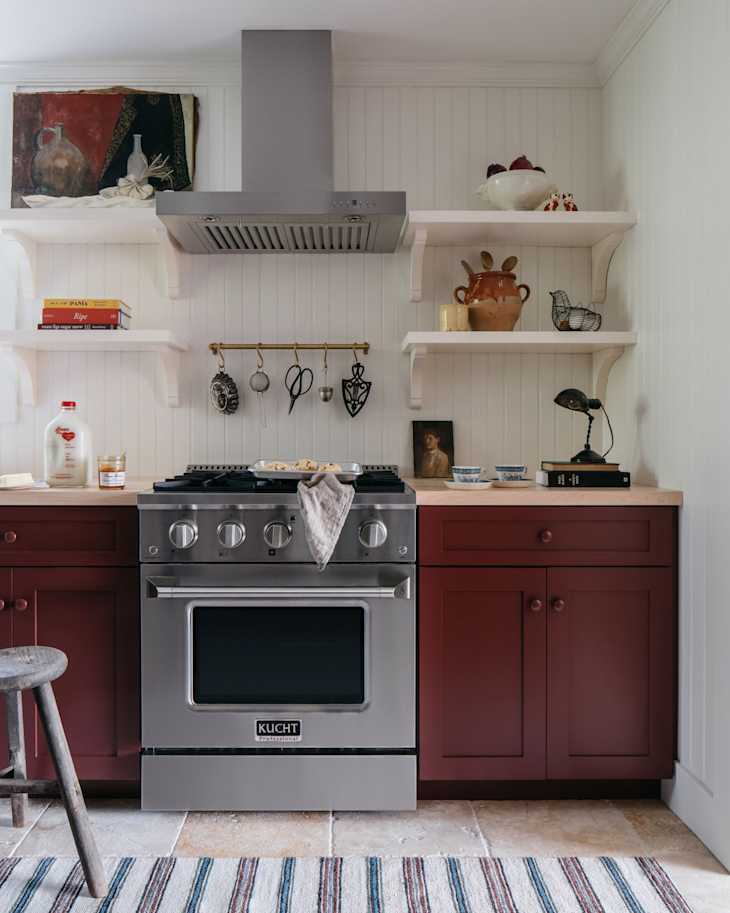 Modern kitchen with burgundy cabinets, stainless steel stove, open shelves, and decorative items.