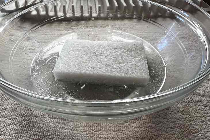 A rectangular sponge submerged in water inside a clear glass bowl.