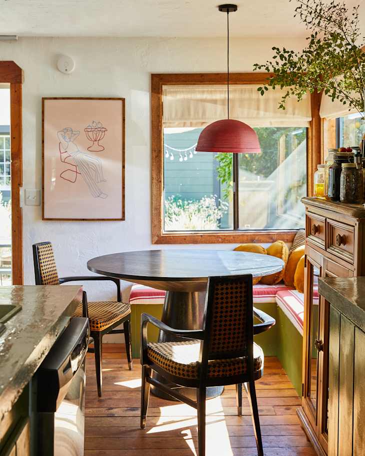 Cozy dining area with a round table, patterned chairs, a red pendant light, and a window seat with cushions.