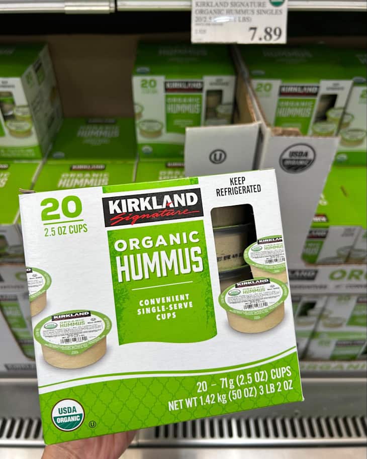 Pack of 20 single-serve cups of organic hummus with green packaging, displayed in a grocery store.