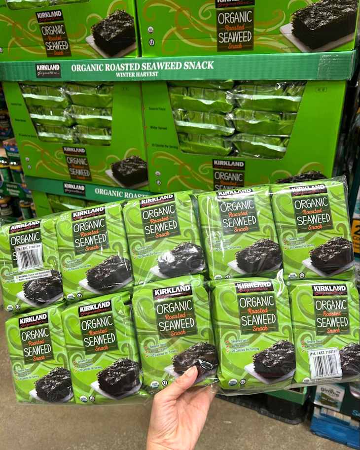 Packaged organic roasted seaweed snacks in green packaging, held by a hand, with multiple boxes stacked in the background.