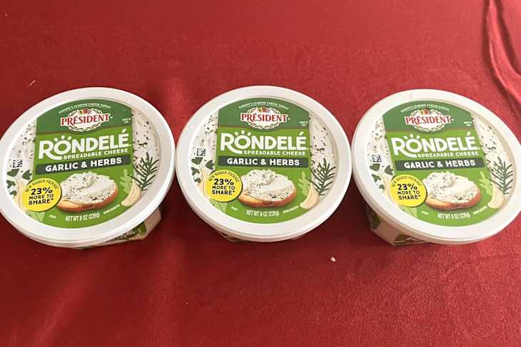 Three containers of Président Rondelé spreadable cheese in Garlic & Herbs flavor, placed on a red tablecloth.