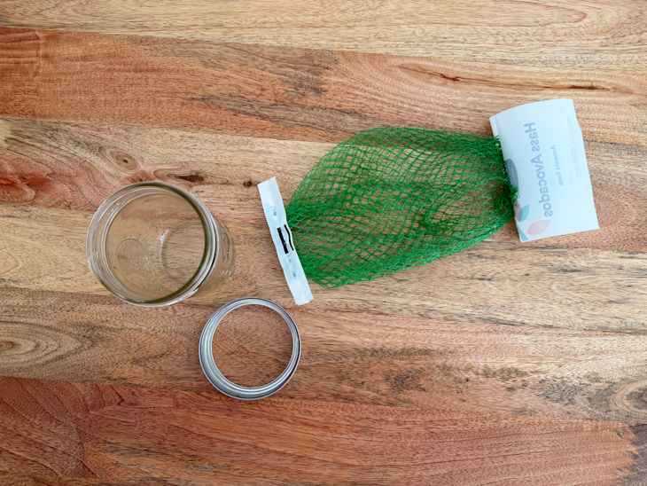 Glass jar with a metal lid, green mesh bag for avocados, and a wooden surface.