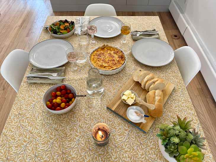 Table set for dinner party (dishes, food, glasses of wine) on oilcloth tablecloth