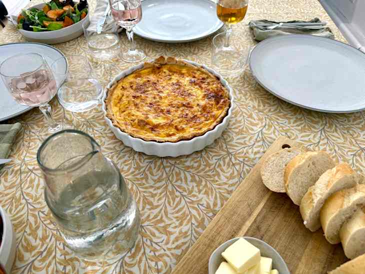 Table set for dinner party (dishes, food, glasses of wine) on oilcloth tablecloth