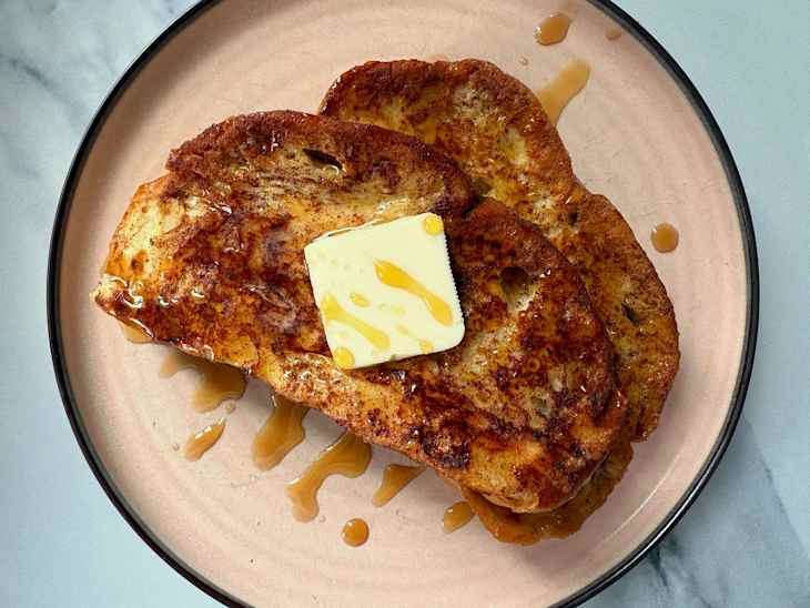 Two slices of French toast topped with a pat of butter and drizzled with syrup on a pink plate.