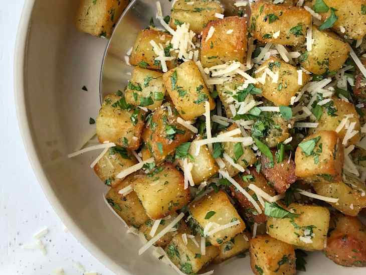 Crispy golden potato cubes garnished with fresh herbs and grated cheese in a bowl.