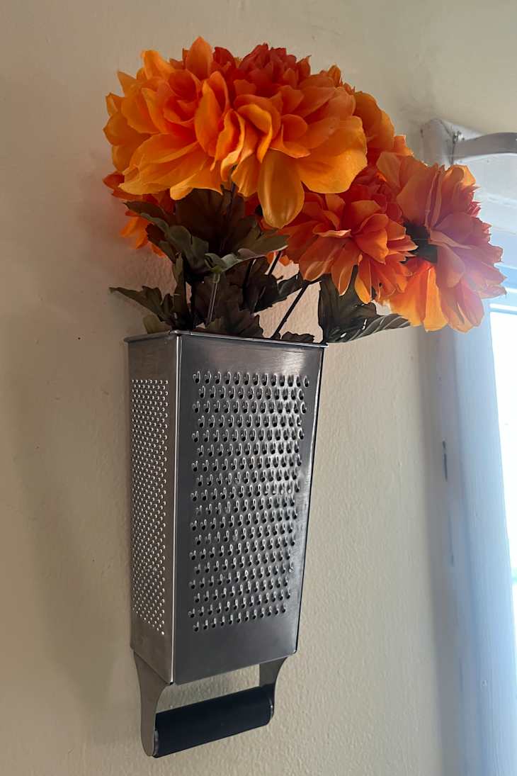A stainless steel grater mounted on a wall, holding orange flowers.