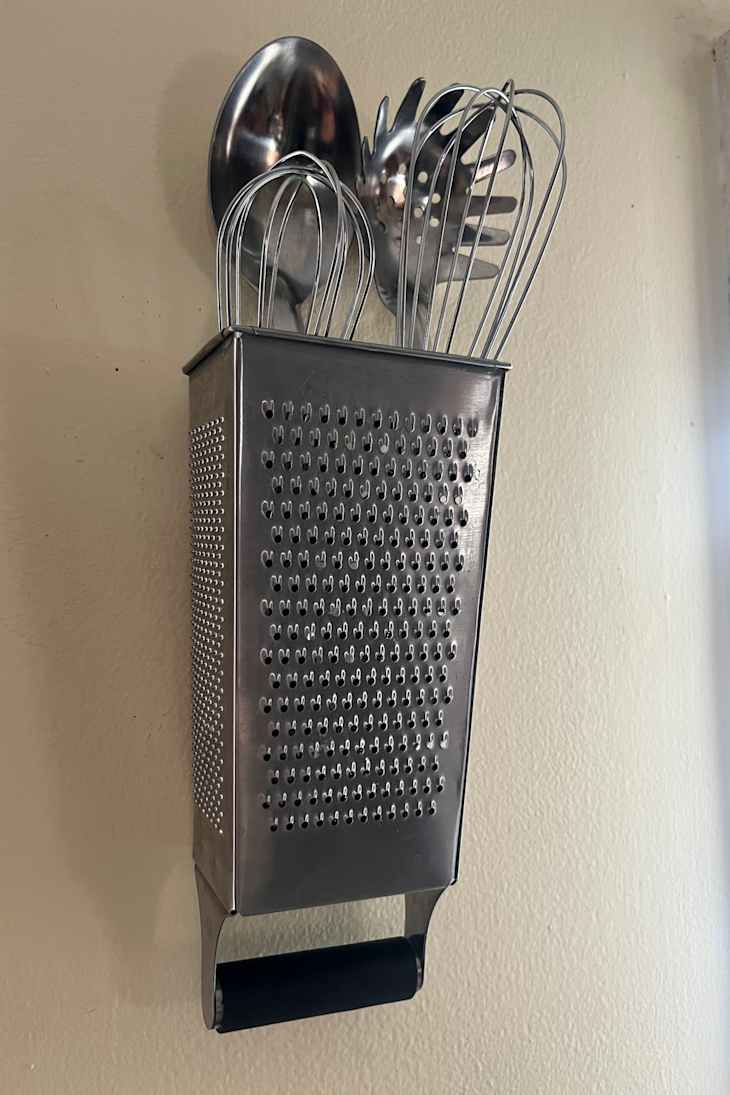 A stainless steel grater mounted on a wall, holding kitchen supplies.