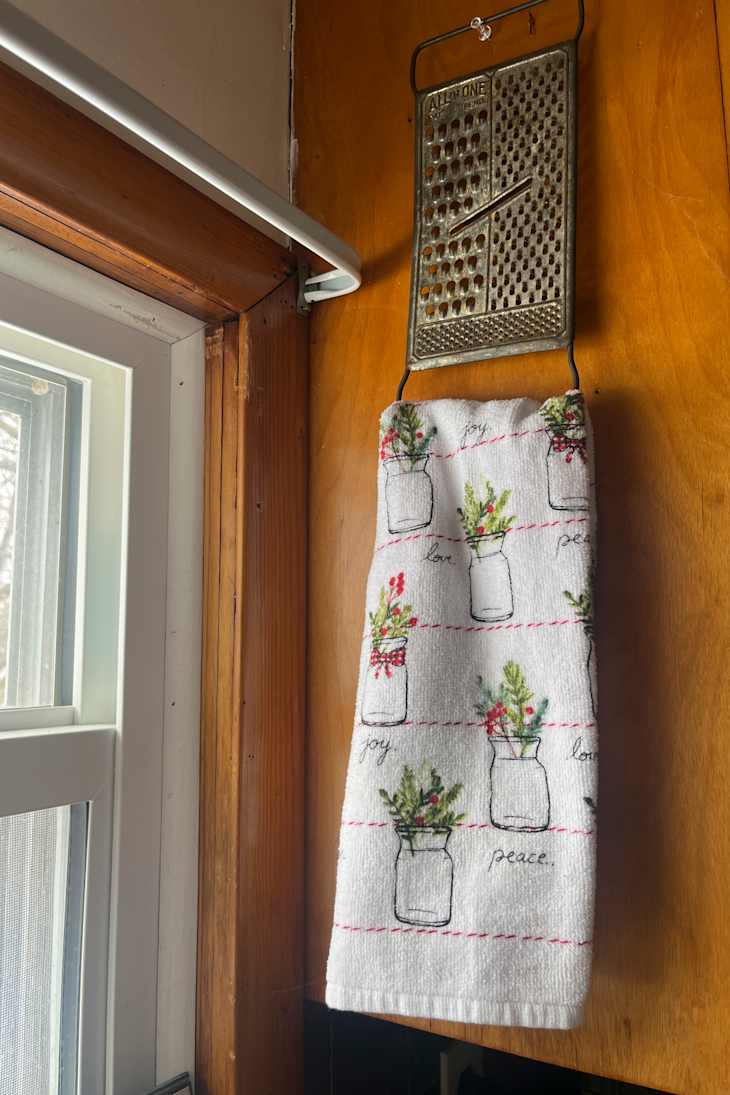 A decorative kitchen towel with jar illustrations and the words "joy," "love," and "peace," hanging near a window.