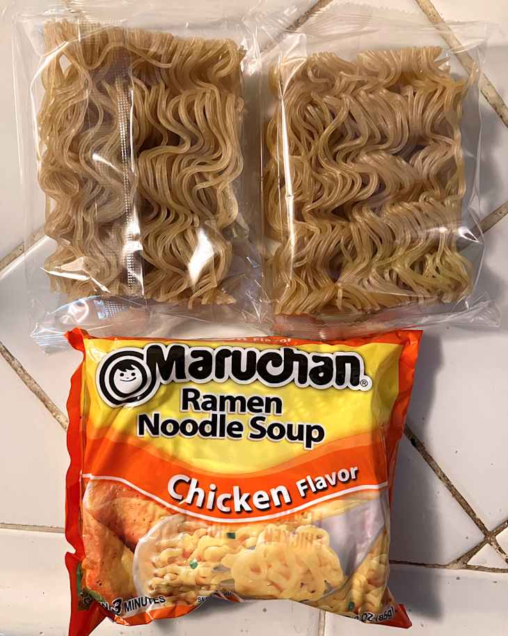 Two packages of ramen noodles and a chicken flavor soup packet on a tiled surface.