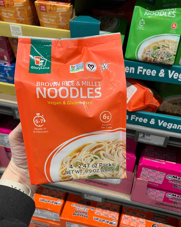 Orange packaging of GloryLand Brown Rice & Millet Noodles, labeled vegan and gluten-free, displayed on a store shelf.