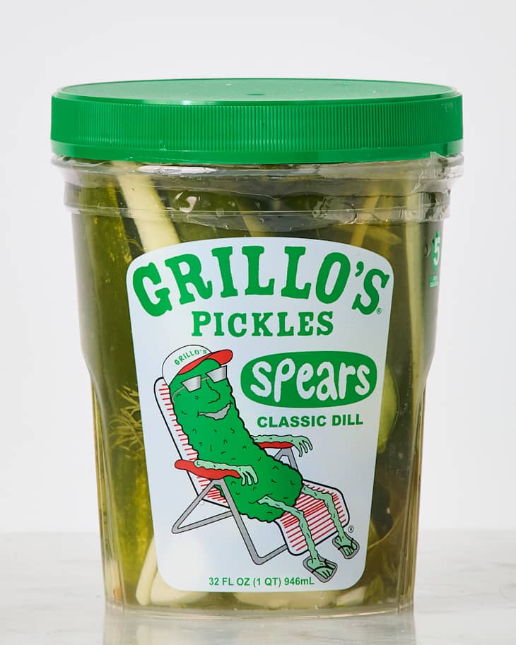 Container of Grillo's Classic Dill Pickles with a cartoon pickle character on the label, sitting in a chair.