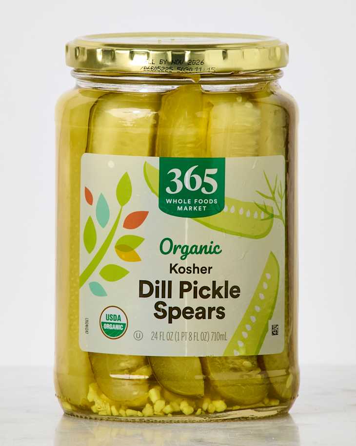 Jar of organic kosher dill pickle spears with a green label and gold lid, showcasing pickles and spices inside.