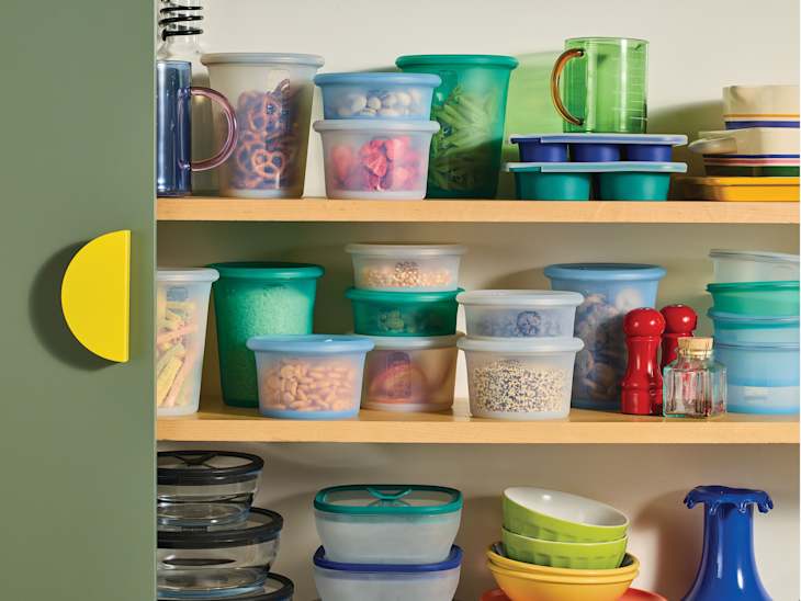 Colorful kitchen storage containers and bowls on wooden shelves, with a green cabinet door partially open.