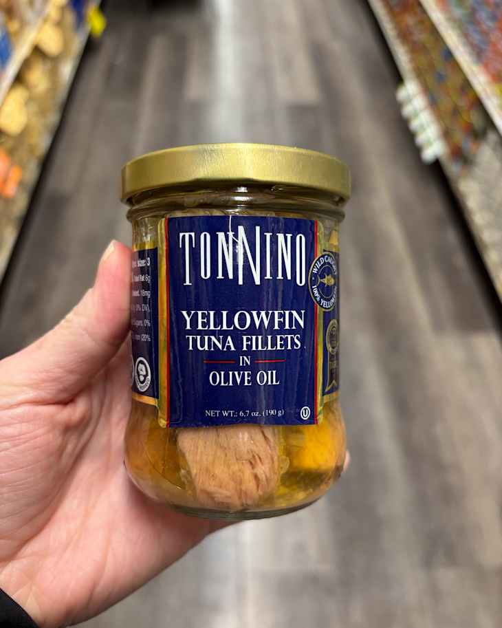 Someone holding a jar of Tonnino yellowfin tuna fillets.