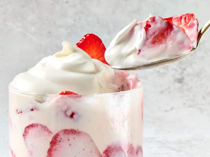 Creamy dessert in a glass with layers of strawberries and whipped cream, with a spoonful ready to serve.