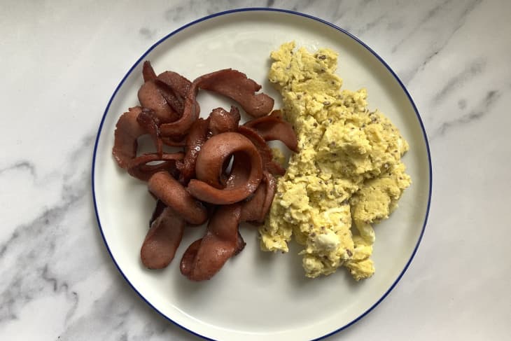 Hot dog bacon cooked next to eggs on a plate.