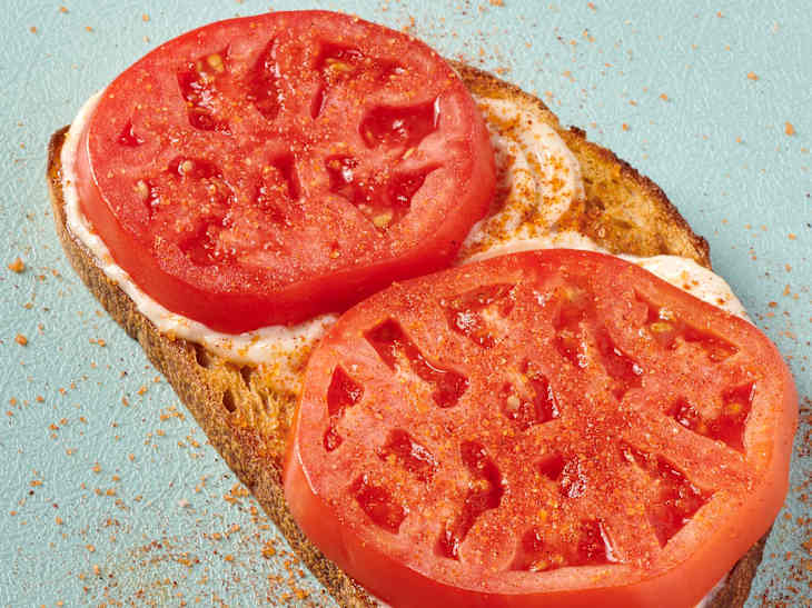 photo of tomato toast with mayonnaise, sliced tomatoes, and smoked salt on a blue cutting board