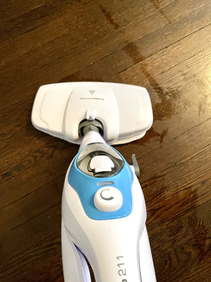 Steam mop cleaning a wooden floor with visible water streaks.